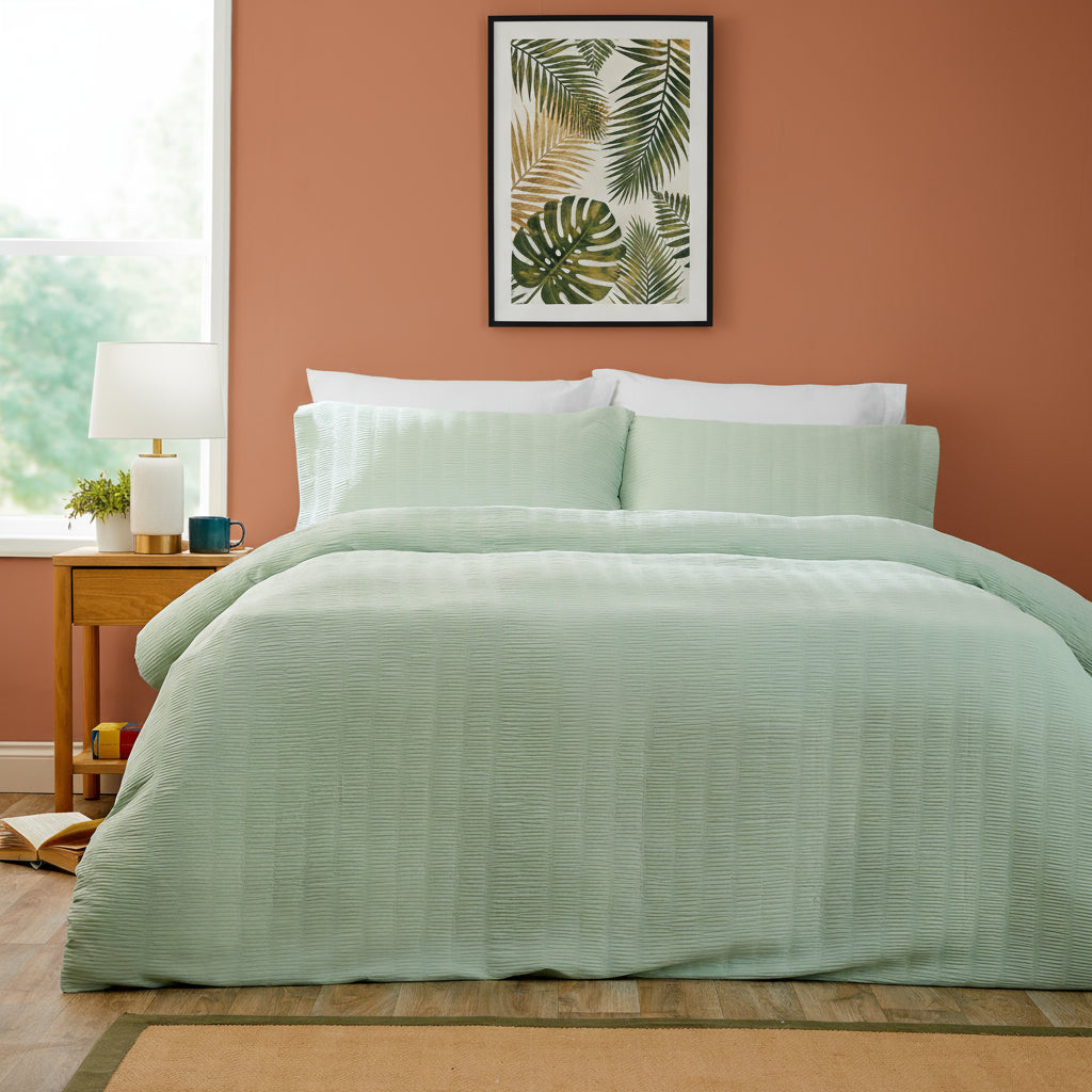 Bedroom with a bed covered in light green bedding, a side table with decor items, and a abstract art piece on the wall.
