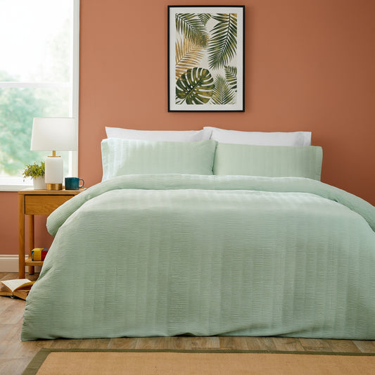 Bedroom with a bed covered in light green bedding, a side table with decor items, and a abstract art piece on the wall.